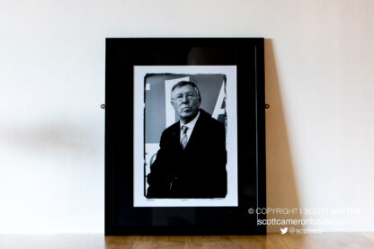 A photograph, of a framed black and white portrait of Sir Alex Ferguson in the dugout at Pittodrie Stadium, Aberdeen, Scotland.