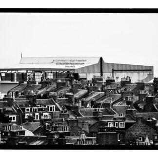 A black and white photograph of Pittodrie Stadium with houses in the foreground with the stadium rising in the background.
