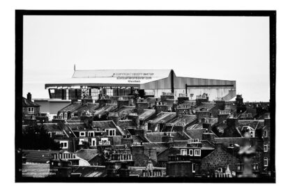A black and white photograph of Pittodrie Stadium with houses in the foreground with the stadium rising in the background.