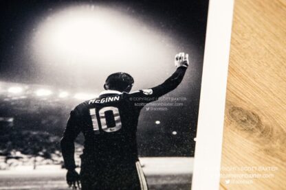 Black and white image of Niall Mcginn from behind while taking a corner on a rainy evening.