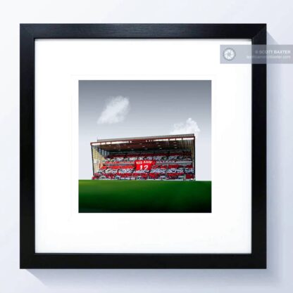 A photograph of Aberdeen Football Club - Pittodrie Stadium by Aberdeen photographer Scott Cameron Baxter. The image is taken from the merkland road end, towards the Richard Donald Stand. The brass is green and the stand is full with supporters holding a RED ARMY banner shaped like a t-shirt. it is red. the fans have mixed red and white paper qurares all aroudn the stand. There are two clouds above the stand and the sky is gray.. This photograph is shown in a mock up black square frame.